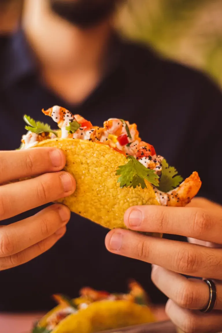Pessoa segurando um taco recheado com carne, molho, coentro e cebola