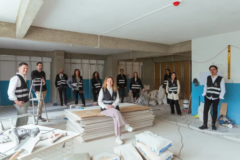 Grupo de pessoas dentro de uma obra de construção civil, usando coletes de segurança, posando para uma foto, com...