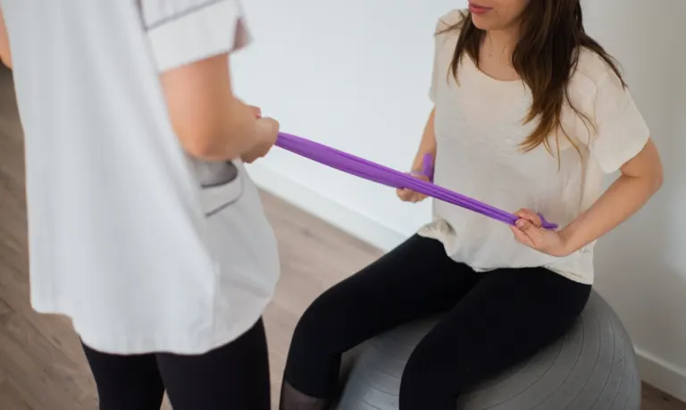 Paciente realizando fisioterapia com faixa elástica conduzida por fisioterapeuta em consultório.