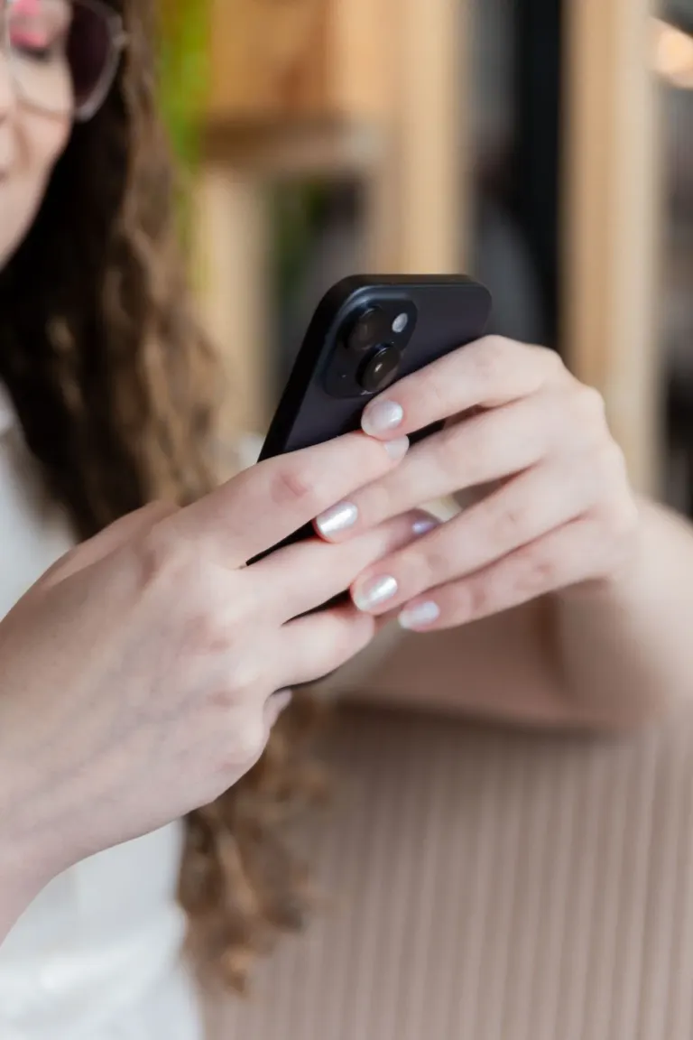 Pessoa segurando um telefone inteligente preto com duas câmeras na parte de trás, unhas com esmalte branco brillante,...