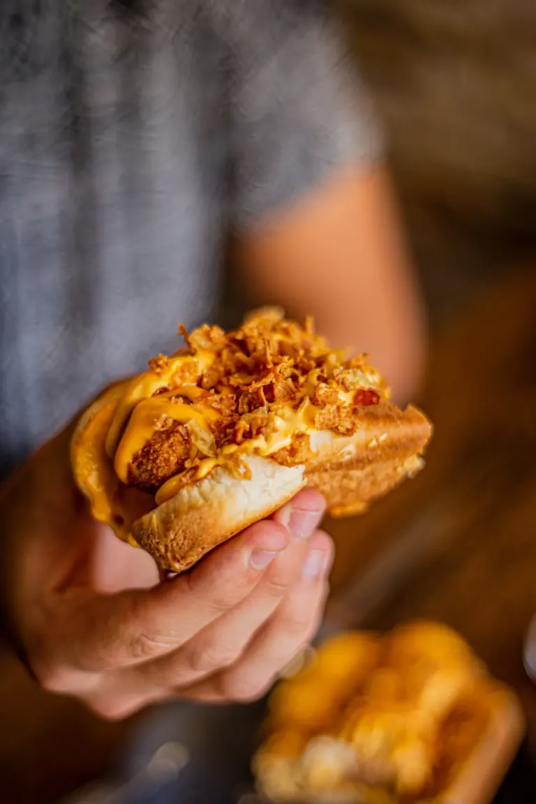 Pessoa segurando um pão recheado com frango, milho, queijo, molho especial e farofa crocante