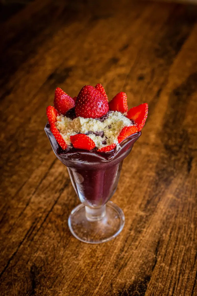 Sorvete de morango com cobertura de chocolate, decorado com morangos frescos e pedaços de biscoito, em taça de vidro...