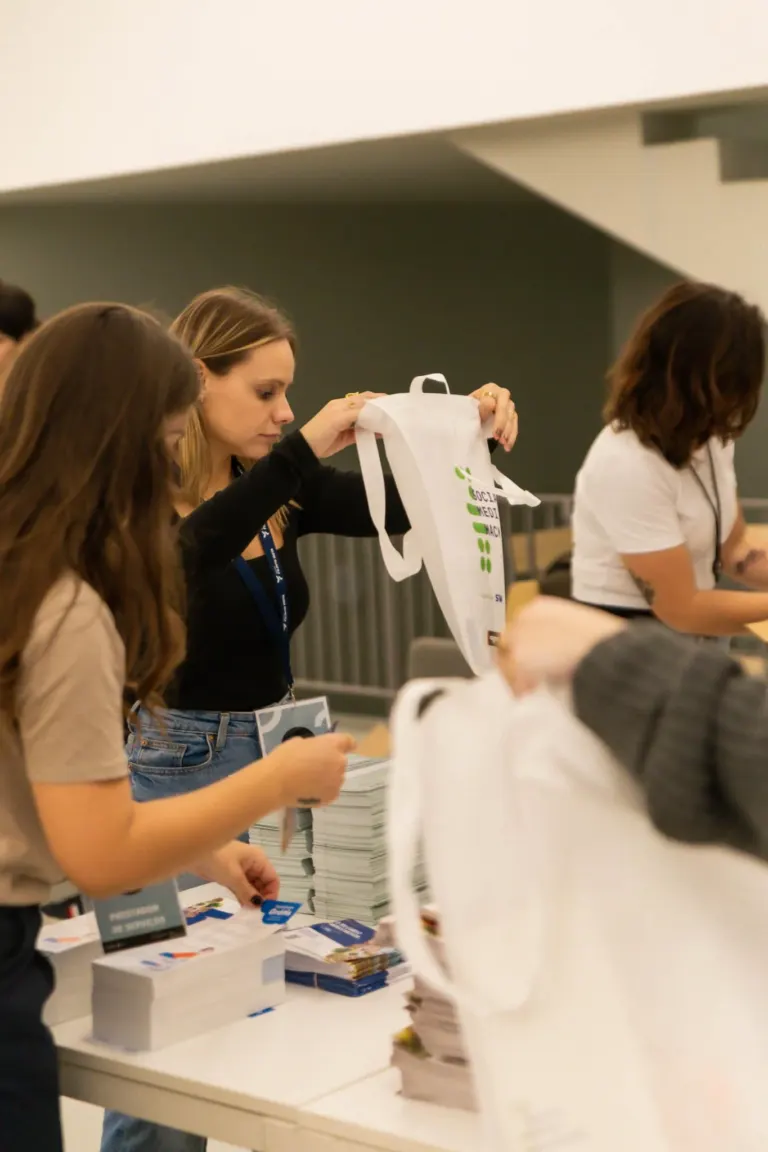 Mulheres organizando materiais em uma mesa durante um evento.