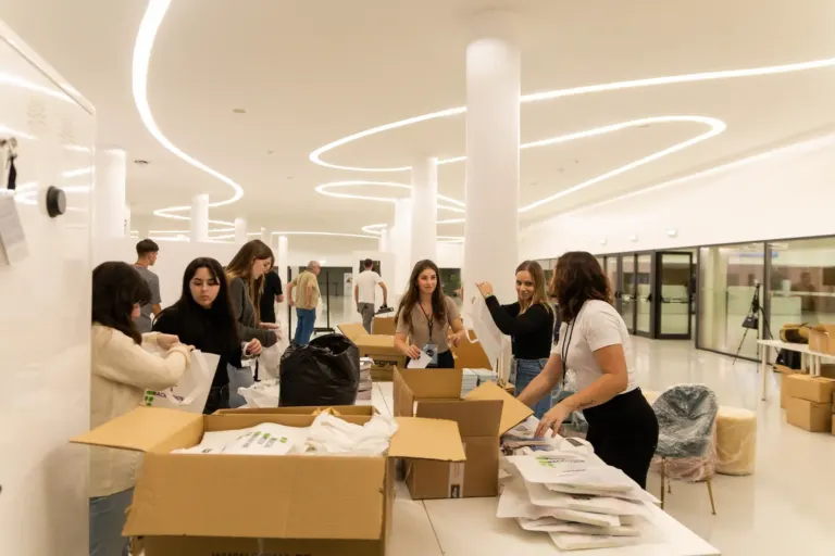 Grupo de pessoas organizando materiais em uma mesa dentro de um espaço moderno com iluminação de teto em curvas.