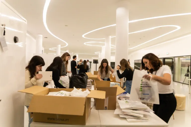 Grupo de pessoas organizando brindes e materiais em uma mesa em um espaço moderno e bem iluminado.