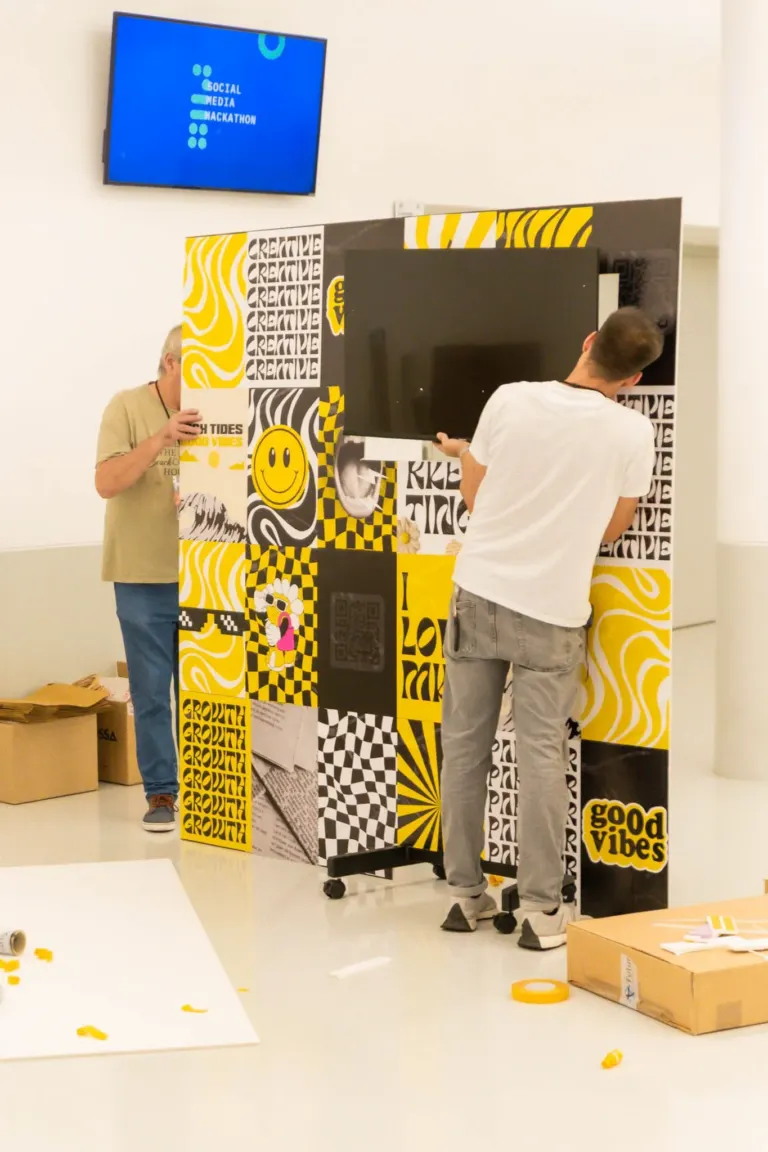 Pessoa ajustando um painel decorativo colorido em branco, amarelo, preto e cinza com palavras como "creative" e "good...