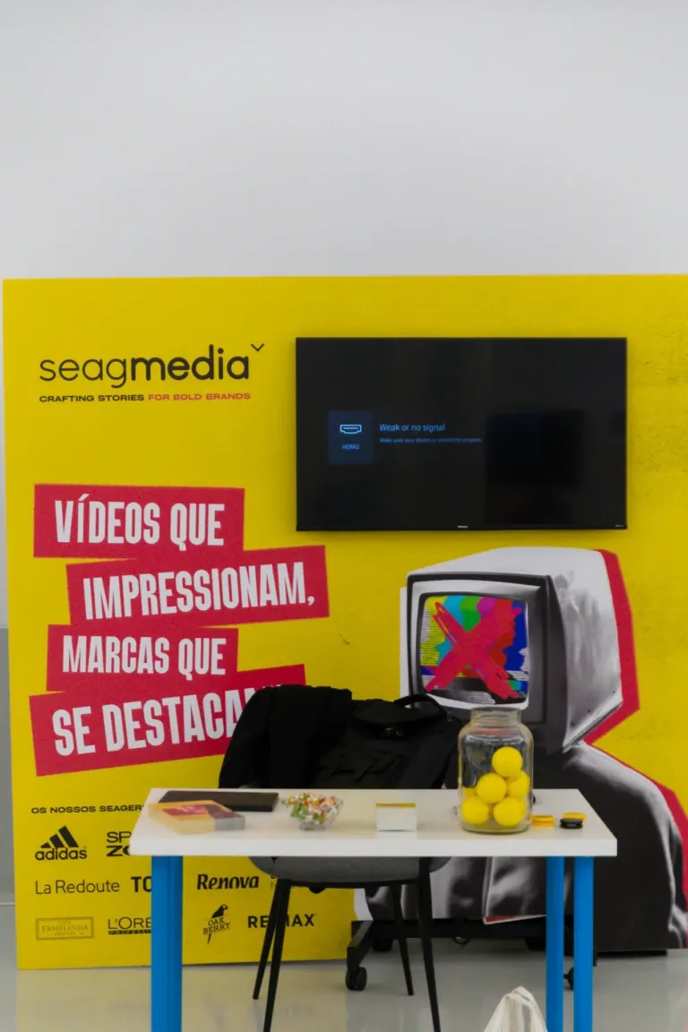 Vitrine com pôster amarelo de publicidade da Seag Media, mostrando uma TV com mensagem de sinal fraco, e uma imagem de um...