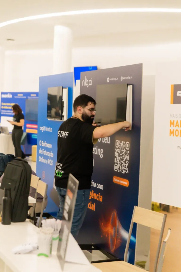 Homem ajustando uma tela de exibição em uma feira de tecnologia, com banner ao fundo destacando software de financiamento...