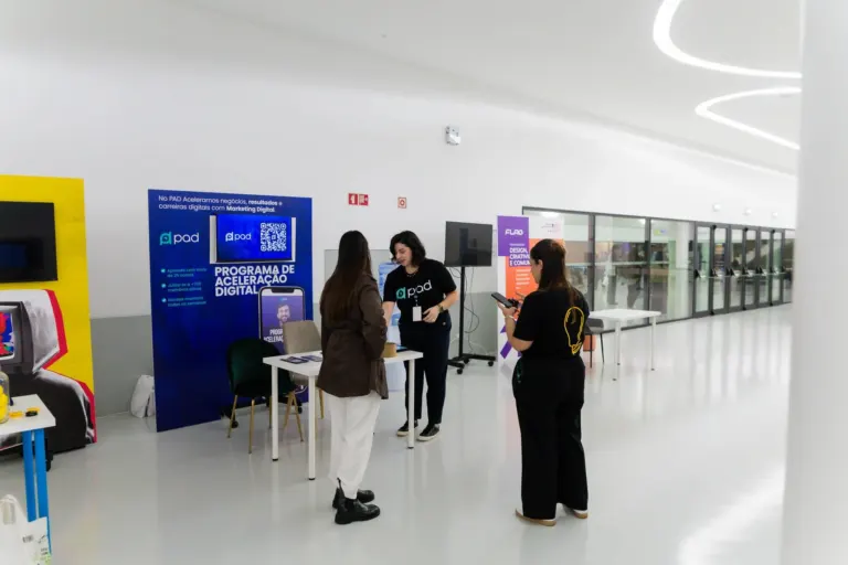 Três pessoas interagindo em uma estação de informações no interior de um prédio com paredes brancas e piso claro, com...
