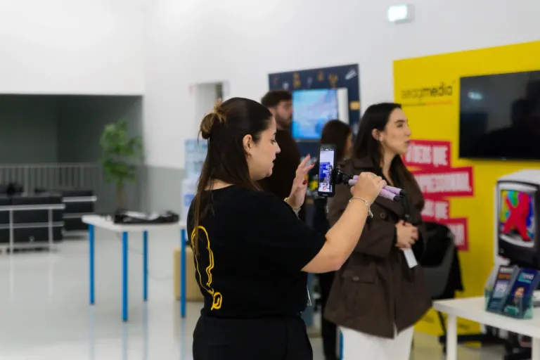 Mulher usando celular com tripé, outras pessoas observando em ambiente de loja ou centro de atendimento