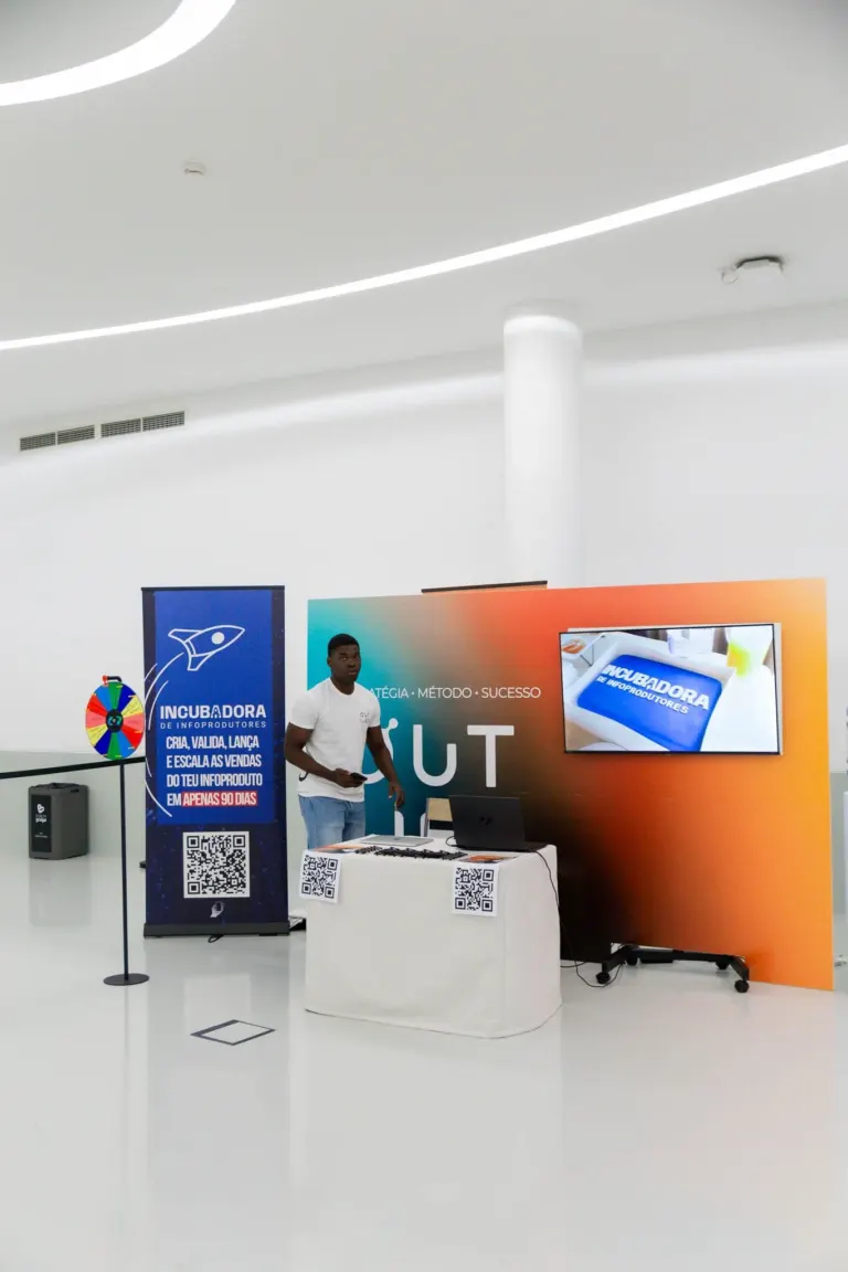 Pessoa em um stand de evento com banner de inscrição, tela digital exibindo um tablet com a palavra 'Incubadora' e uma...