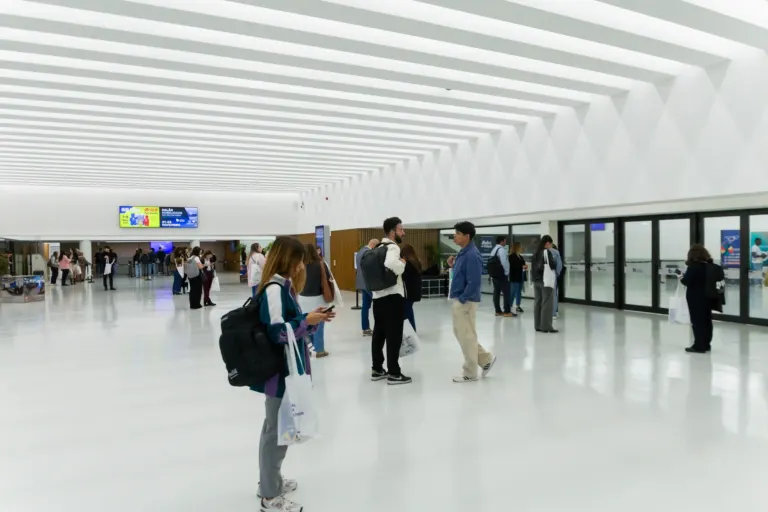 Interior de um aeroporto com dezenas de pessoas aguardando próximo às portas de embarque. Pessoas interagindo, usando...