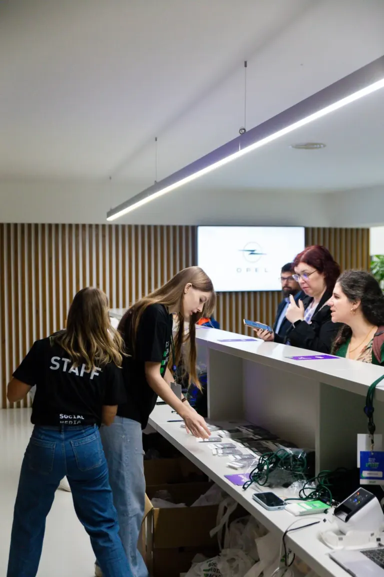 Ponto de recepção em uma conferência ou evento, com várias pessoas interagindo na área de credenciamento ou inscrição.