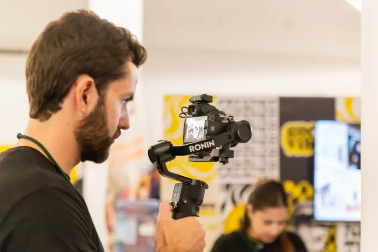 Homem com barba ajustando câmera fotográfica em evento interno.