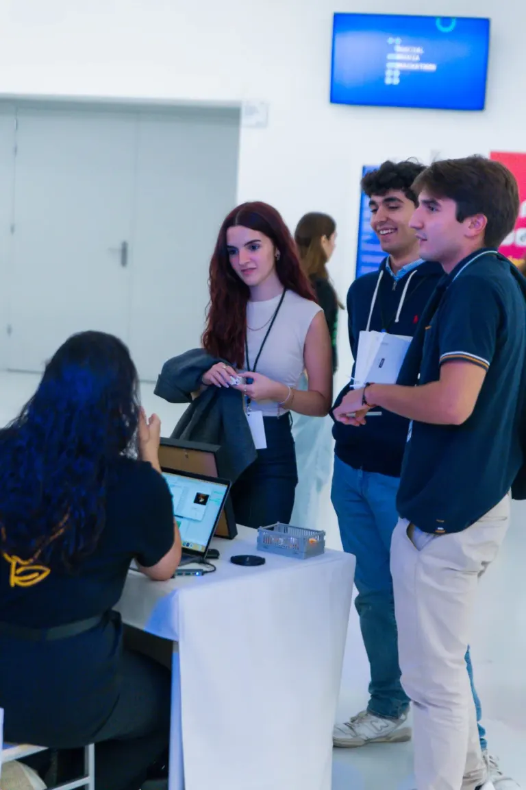 Grupo de pessoas em pé ao redor de uma mesa, conversando, em um evento ou conferência. Uma pessoa está usando um laptop...