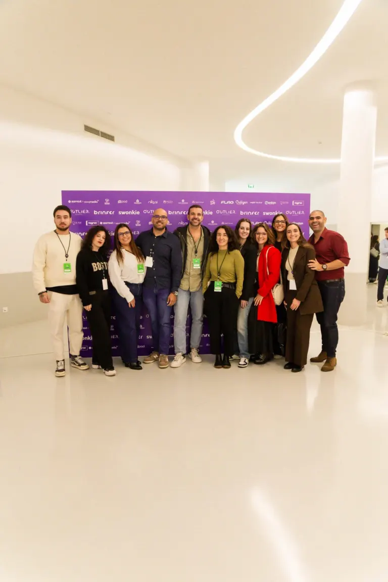 Grupo de pessoas posando para uma foto em linha com fundo roxo com logos e nomes de patrocinadores.
