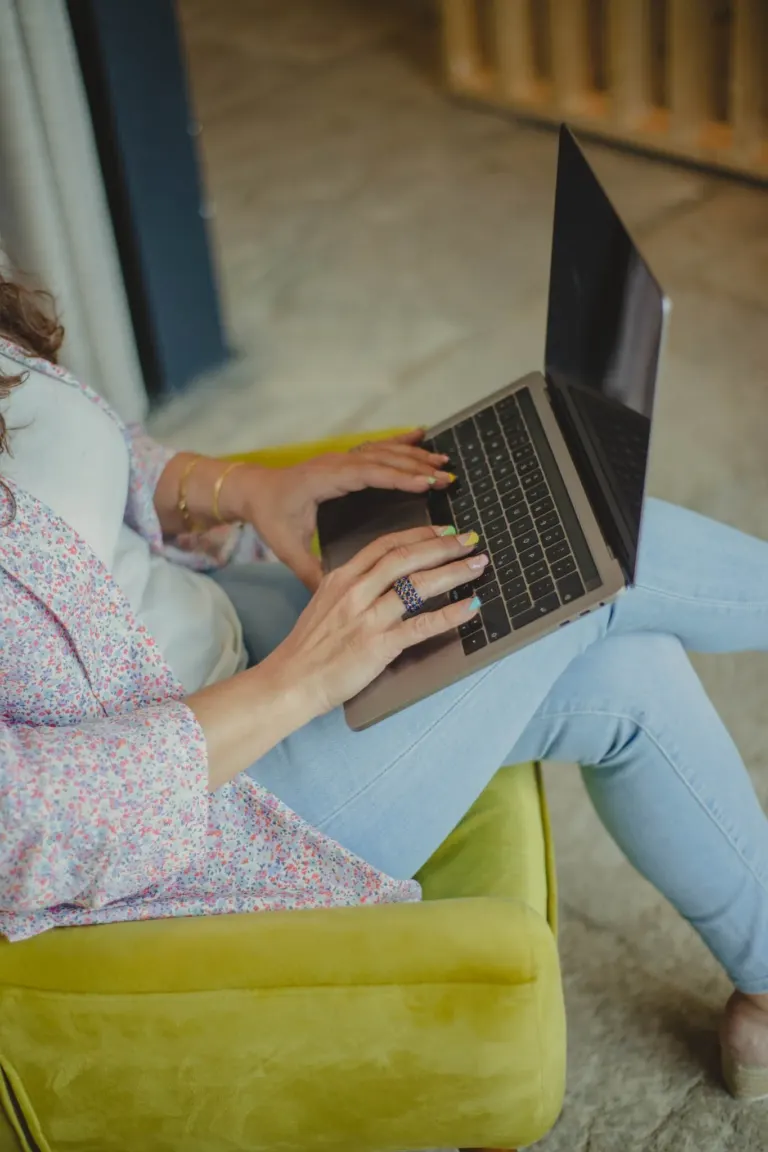 Pessoa usando um laptop enquanto está sentada em um sofá amarelo.